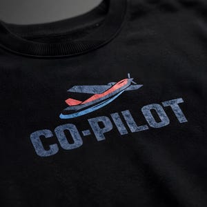 Könnte beinhalten: Schwarzes Sweatshirt mit Rundhalsausschnitt und einem verblassten Flugzeug-Motiv sowie dem Text "CO-PILOT" in Blau. Das Flugzeugdesign weist rote, blaue und graue Farben auf. Ein lässiges, bequemes Oberteil für Luftfahrt-Enthusiasten.