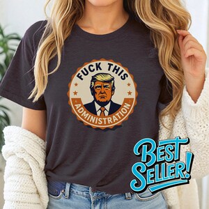 Może przedstawiać: Szary t-shirt z okrągłym nadrukiem przedstawiającym karykaturę Donalda Trumpa z tekstem "F**K THIS ADMINISTRATION".