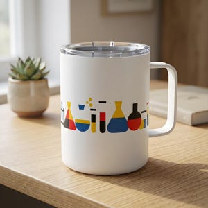 Può includere: Tazza da viaggio bianca con manico e coperchio trasparente. La tazza presenta un design colorato di fiasche e beute da laboratorio in rosso, giallo, blu e nero. La tazza è appoggiata su una superficie di legno.