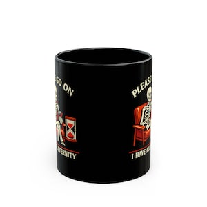 May include: A black ceramic mug featuring a graphic of a skeleton sitting in a red armchair, holding a book, with an hourglass nearby. The text reads: PLEASE GO ON I HAVE ALL ETERNITY. The design is printed on the side of the cylindrical vessel.