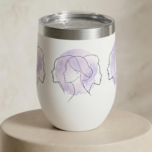 Peut inclure: Gobelet à vin isotherme blanc avec un bord et un couvercle argentés. Le gobelet présente un motif de profils de femmes en dessin au trait noir, sur un fond aquarelle violet doux. Le motif est répété autour du gobelet.