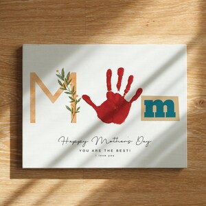 May include: A white card with the word "MOM" in gold and teal letters. The "O" is a red handprint. The card says "Happy Mother's Day You Are The Best! I love you."