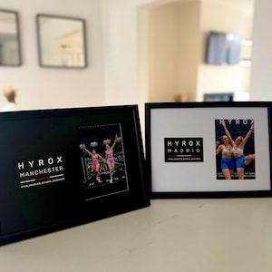 May include: Two black framed photos. One displays "HYROX MANCHESTER" and a photo of two women in pink athletic wear. The other shows "HYROX MADRID" and a photo of two women in blue athletic wear.