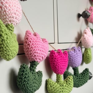 Könnte beinhalten: Handgefertigte Häkelgirlande mit rosa, pinken und lila Tulpen mit grünen Blättern. Die Blumen sind mit einem Naturfaden aufgereiht und bilden einen dekorativen floralen Akzent.