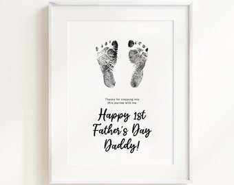 May include: A framed print with a black and white baby footprint design. The text reads "Thanks for stepping into this journey with me. Happy 1st Father's Day Daddy!"