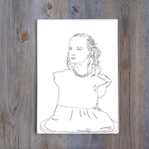 May include: A black and white line drawing of a person wearing a dress and a necklace. The artwork is on a white background, with a wooden surface in the background.