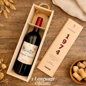 Peut inclure: Une bouteille de vin rouge Chateau Bessan Segur 2015 dans un coffret cadeau en bois clair. Le couvercle coulissant porte l'inscription Millesime 1974, une phrase sur le vin qui se bonifie avec l'âge, Joyeux Anniversaire et le nom Lucas en rouge.