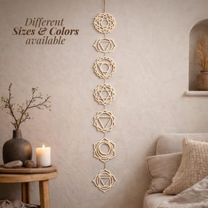 Peut inclure: Une décoration murale verticale composée de sept symboles de chakras en bois découpés au laser et reliés par une fine ficelle. Les ornements en bois clair présentent des motifs géométriques complexes. Le texte "Different Sizes & Colors available" est visible.