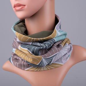 Puede incluir: Un calentador de cuello colorido con un patrón geométrico en tonos marrones, verdes y amarillos. El calentador de cuello está hecho de una tela suave y elástica, perfecto para mantenerse caliente en invierno.