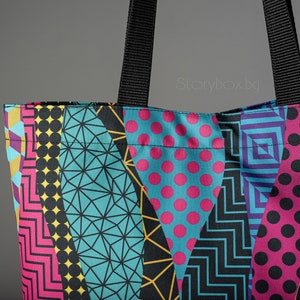 Puede incluir: Una bolsa de tela colorida con un patr&oacute;n geom&eacute;trico en negro, amarillo, rosa, azul y blanco. La bolsa tiene asas negras.