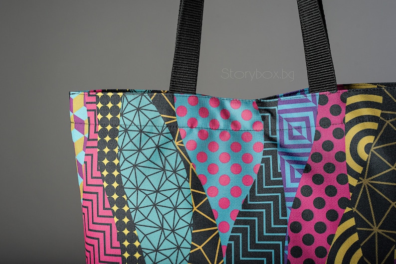 Puede incluir: Una bolsa de tela colorida con un patr&oacute;n geom&eacute;trico en negro, amarillo, rosa, azul y blanco. La bolsa tiene asas negras.