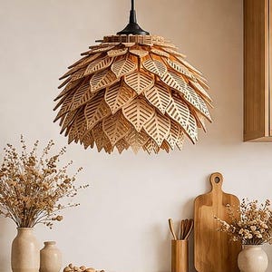 Peut inclure: Un luminaire suspendu en bois clair en forme de feuilles. Il est suspendu par un cordon noir. La cuisine comprend une planche à découper en bois, des vases et une assiette de noix.