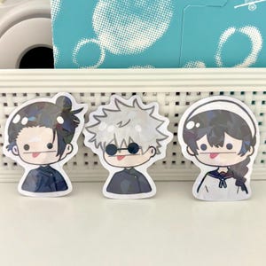 May include: Three cartoon character stickers with black hair, white hair, and black hair. The characters are all wearing different outfits and have different expressions. The stickers are on a white background.
