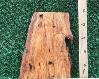 Op de afbeelding: Een groot stuk olijfhout met een natuurlijke rand en een knoop. Het hout is lichtbruin van kleur met donkerbruine strepen. Het hout is ongeveer 50 cm lang en 38 cm breed.