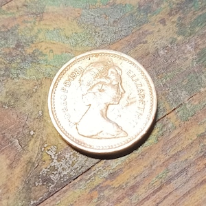 Peut inclure: Une pièce d'argent avec le profil de la reine Élisabeth II et le texte "ELIZABETH II" et "ONE POUND" sur la pièce.