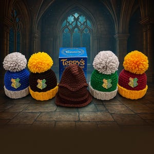 May include: Five handmade crochet hats with pom-poms, featuring the Hogwarts crest. The hats are blue, brown, green, and red, with yellow and grey accents. A box of Terry's Chocolate Orange is in the background.