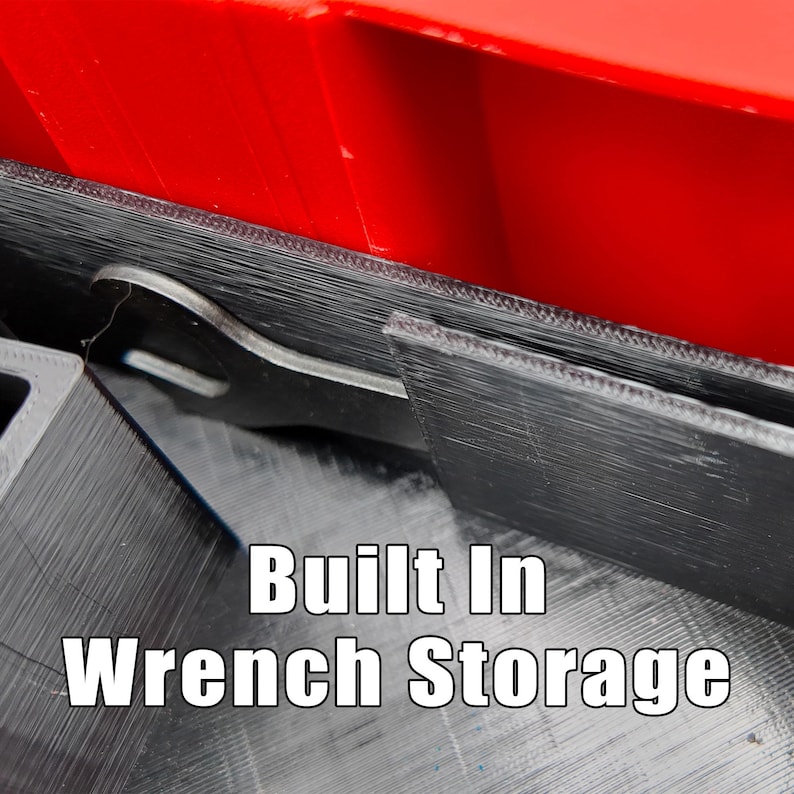 May include: Close-up of a black wrench storage compartment with a red top. The text "Built In Wrench Storage" is displayed in white. The compartment appears to be made of a 3D-printed material.
