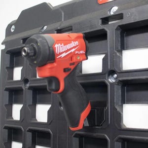 May include: A red and black Milwaukee FUEL impact driver mounted on a black storage panel. The tool has a black handle and the Milwaukee logo in white. The storage panel has a grid-like design.
