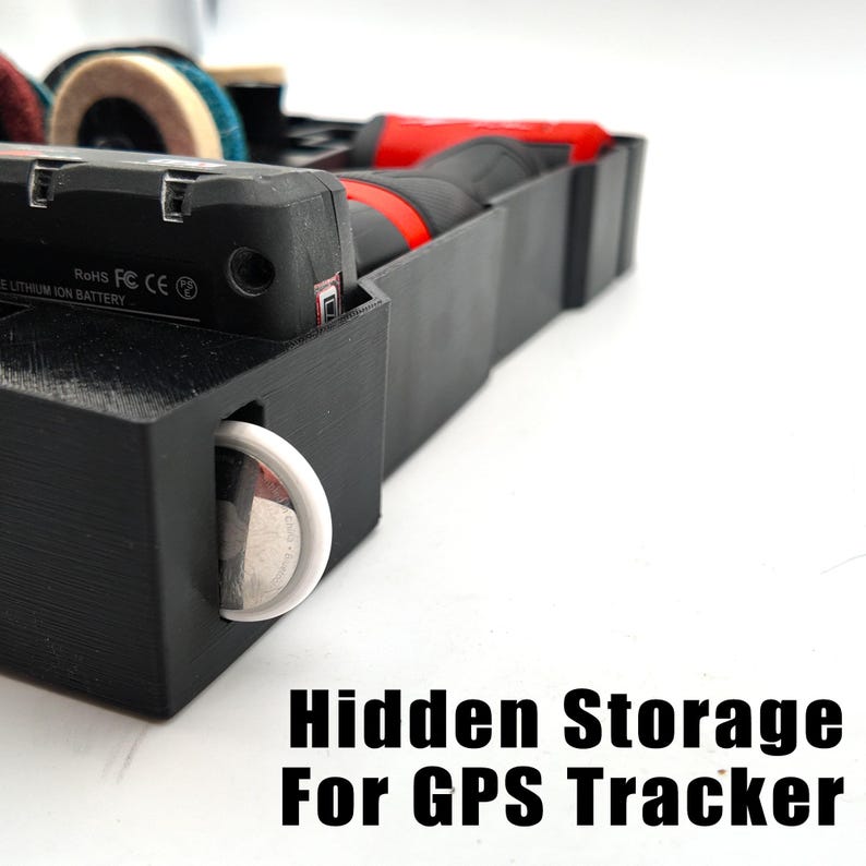May include: Black plastic hidden storage container for a GPS tracker. The container has a compartment for the tracker and a slot for a white circular object. The text "Hidden Storage For GPS Tracker" is at the bottom.