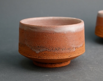 May include: A small, brown ceramic bowl with a white glaze on the rim. The bowl has a textured surface and a slightly flared lip.