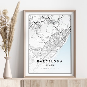 Op de afbeelding: Een zwart-witte kaartprint van Barcelona, Spanje, in een lichtbruin frame. De kaart toont de straten en bezienswaardigheden van de stad. De tekst "Barcelona, Spanje" en de coördinaten "41.3874° N, 2.1666° E" zijn onder de kaart afgedrukt.