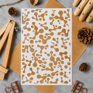 May include: A rectangular white stencil featuring a repeating organic pattern of interconnected blobs and circular shapes. The design consists of various fluid, amoeba-like cutouts distributed across the entire surface of the flat sheet.