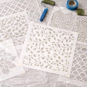 a collection of stencils and tools, including a paint roller, paintbrush, and tape, arranged on a white surface.