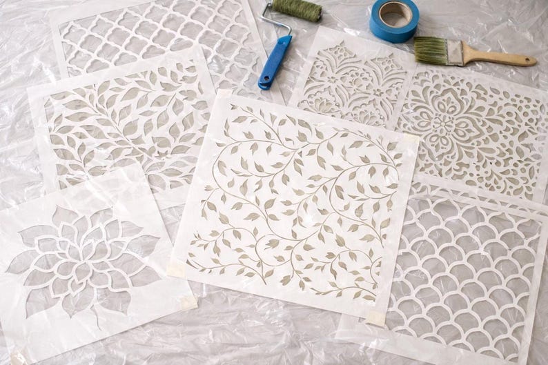 a collection of stencils and tools, including a paint roller, paintbrush, and tape, arranged on a white surface.