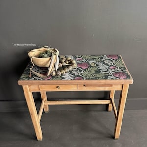 a wooden table with a floral patterned top, displaying various items such as a bowl, a necklace, and a plant.