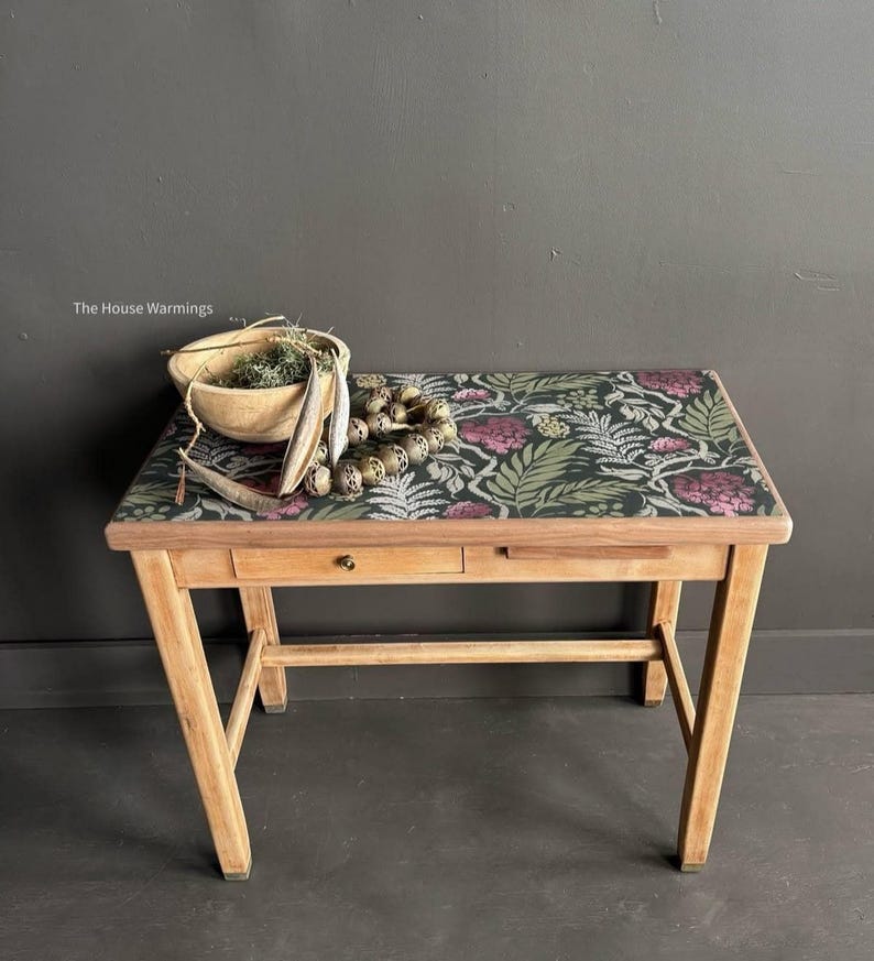a wooden table with a floral patterned top, displaying various items such as a bowl, a necklace, and a plant.