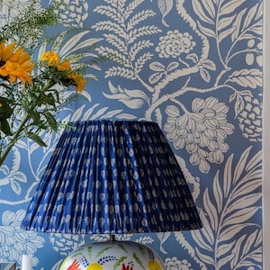 a blue lamp shade with a white pattern, placed on a table next to a vase filled with yellow sunflowers. The background has a blue and white floral wallpaper.