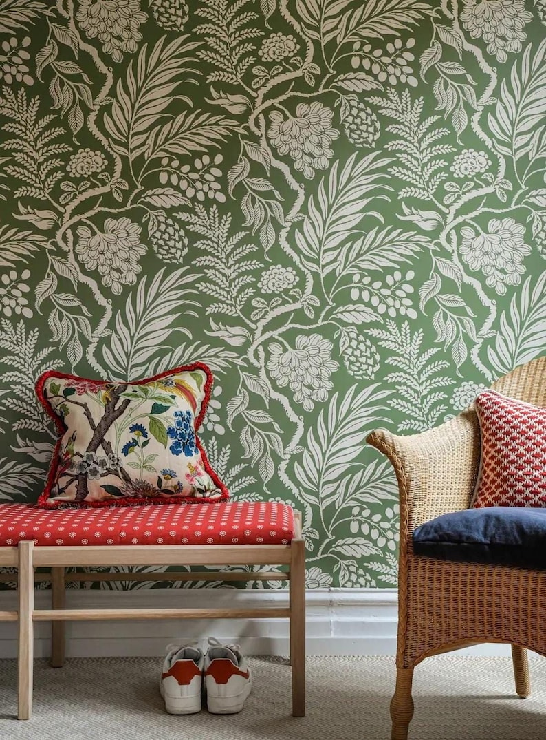 a room with a green floral wallpaper, a red bench with a floral patterned cushion, a wicker chair with a red and white patterned cushion, and a pair of white shoes on the floor.