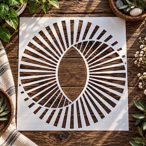 May include: A square white stencil featuring a central geometric design composed of numerous thin, radiating lines that form a circular pattern with an elliptical void in the middle, creating a sunburst effect with sharp, clean-cut edges.