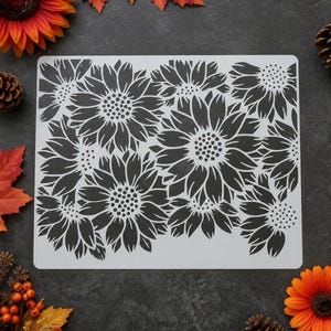 May include: A rectangular stencil featuring a repeating pattern of dark sunflower silhouettes. The design consists of multiple flower heads with detailed central discs and pointed petals, arranged in a dense, overlapping floral composition.