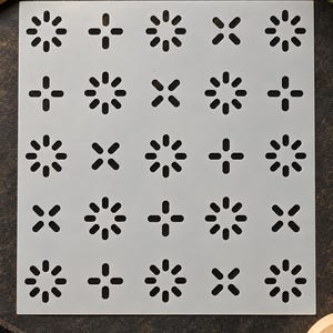 May include: A square, semi-transparent stencil sheet featuring a repeating geometric pattern of alternating eight-petaled flower shapes and four-pointed cross shapes, all composed of small, rounded, oblong cutouts in a grid layout.