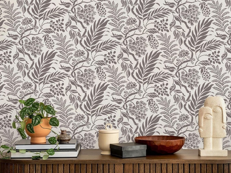 a wooden shelf with various decorative items and a potted plant placed on it. The shelf has a wooden surface and displays a bowl, a vase, a sculpture, and a stack of books. The background is a wall with a floral pattern wallpaper.