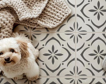 Peut inclure: Un petit chien au pelage clair et duveteux est assis sur un sol composé de carreaux carrés arborant un motif floral gris foncé répétitif sur fond crème. Une épaisse couverture beige en grosse maille recouvre le coin supérieur gauche.