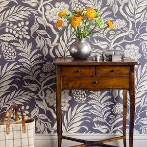 a wooden table with a vase of yellow flowers on top, set against a blue and white floral wallpaper. Next to the table is a white tote bag.