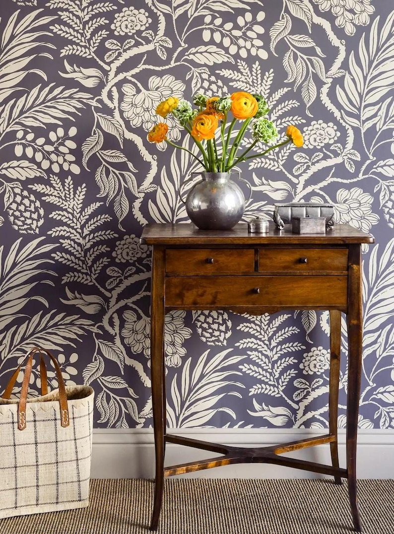 a wooden table with a vase of yellow flowers on top, set against a blue and white floral wallpaper. Next to the table is a white tote bag.