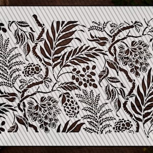 a detailed stencil design with various leafy and floral patterns in shades of brown and black. The design appears to be a stencil for painting or decorating, as it is placed on a white surface and surrounded by other objects such as a bowl and a plant.
