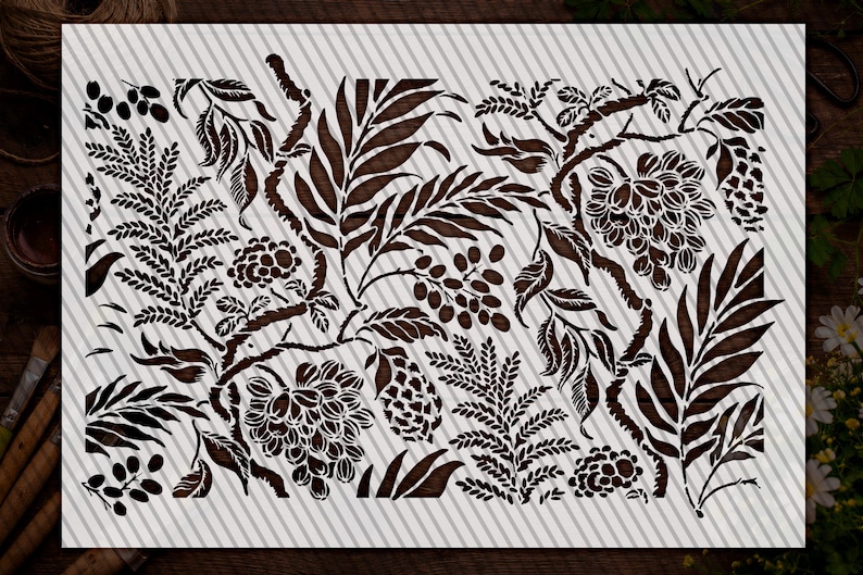 a detailed stencil design with various leafy and floral patterns in shades of brown and black. The design appears to be a stencil for painting or decorating, as it is placed on a white surface and surrounded by other objects such as a bowl and a plant.