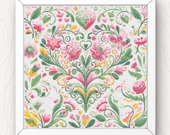 May include: A framed cross-stitch featuring a floral design in pink, green, yellow, and white. The intricate pattern includes stylized flowers, leaves, and heart shapes, all set against a white background. The artwork is displayed in a white frame.