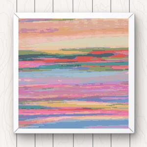 May include: A framed abstract artwork with a pixelated design. The piece displays horizontal bands of colours such as pink, blue, orange, and green, creating a textured, landscape-like effect. The frame is white, and the artwork is displayed against a white wood background.