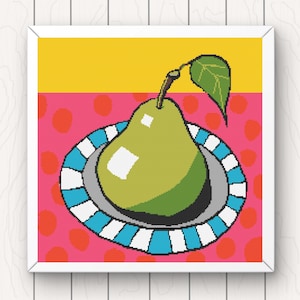 May include: A framed cross-stitch artwork featuring a green pear on a plate. The plate has a blue and white striped rim, set against a pink background with orange polka dots. The top of the artwork is yellow.
