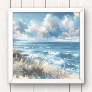 May include: A framed cross-stitch artwork depicting a seascape with a blue sky, white clouds, and a sandy beach with waves crashing on the shore. The foreground features tall, brown grasses.