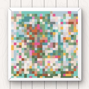 May include: Square framed artwork featuring a colorful pixelated design. The artwork is composed of small squares in various shades of pink, green, orange, and blue. The frame is white, and the background is a light wood grain.
