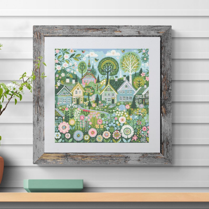 May include: A framed cross-stitch embroidery depicting a whimsical village scene with colorful houses, flowers, and trees. The houses are painted in shades of blue, green, yellow, and pink. The flowers are in bloom and come in a variety of colors, including red, pink, yellow, and purple. The trees are green and lush. The embroidery is set against a light blue background.