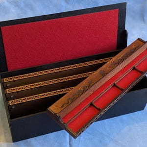 May include: A black wooden box with a red felt interior and several compartments. The box has a decorative wooden tray with red felt lining. The open lid reveals a red felt backing.