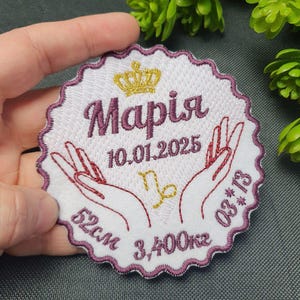 May include: White embroidered patch with a pink border and a gold crown. The patch says "Maria" with the date "10.01.2025" and the zodiac symbol for Capricorn. It also says "52 cm 3,400 kg 08*13".