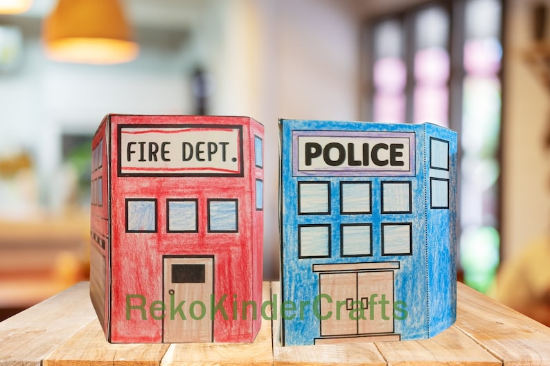 Peut inclure: Deux maisons de jeu en carton, l'une rouge avec "FIRE DEPT." &eacute;crit dessus et l'autre bleue avec "POLICE" &eacute;crit dessus. Les deux ont des fen&ecirc;tres et des portes.